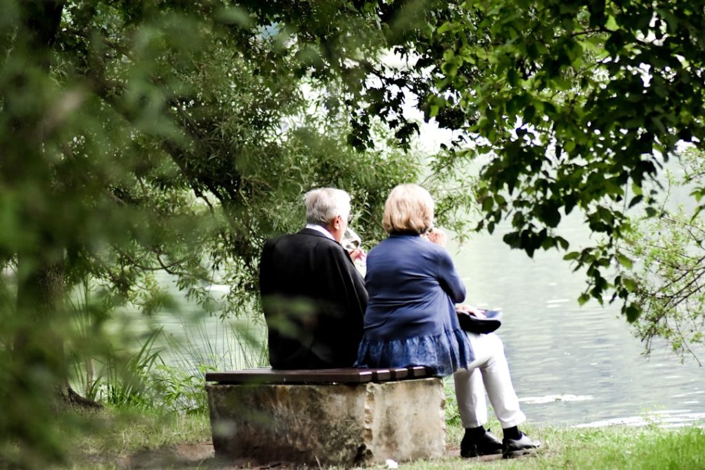 two-people-sitting-on-pavement-facing-on-body-of-water-zla7c39dffk